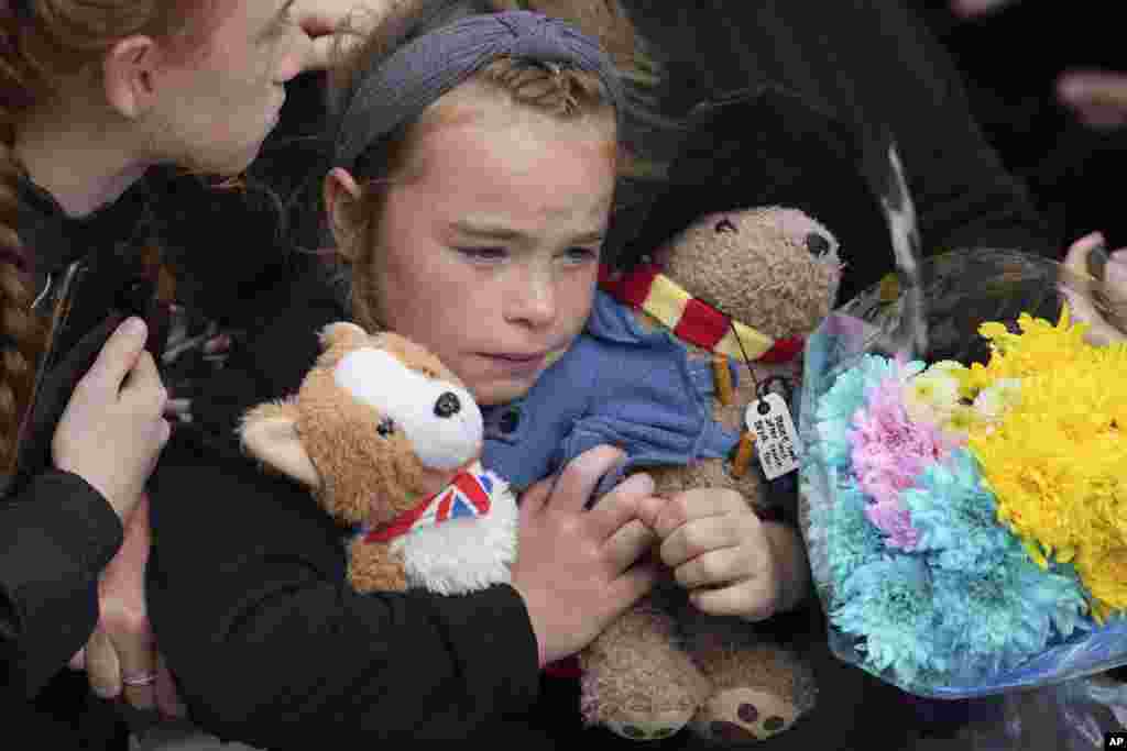 A young girl holds a Paddington bear and a Corgi dog stuffed toys while waiting to watch the Procession of Queen Elizabeth's coffin from the Palace of Holyroodhouse to St. Giles' Cathedral on the Royal Mile in Edinburgh, Scotland.
