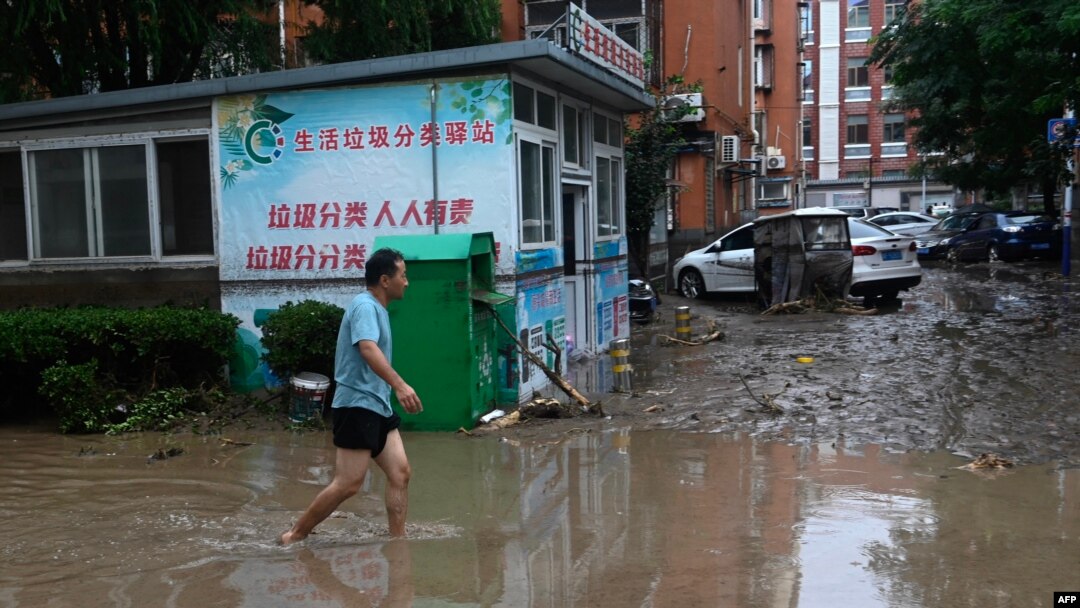 A man walks along a water laden street, after heavy rains in Mentougou district in Beijing on July 31, 2023.