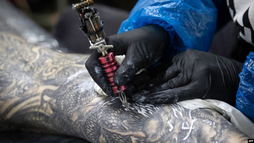 A client has artwork added to his leg at Dragon Tattoo and Body Piercing in Sheffield, England, July 13, 2020. “The dragon always comes with a lot of good meanings, especially for Asian people," says Hong Kong tattoo artist Marcus Yuen. 