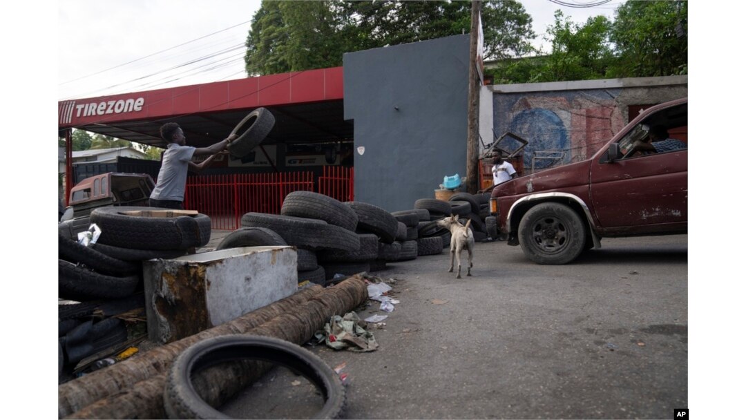FILE - A man throws a tire to make a barricade to close a street at 6 p.m. as part of an initiative to fight gangs seeking to take control of their neighborhood in the Canape Vert area of Port-au-Prince, Haiti, May 31, 2023.