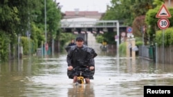 A man rides on a bicycle through floodwaters after heavy rains hit Italy's Emilia-Romagna region, in Lugo, Italy, May 19, 2023. 