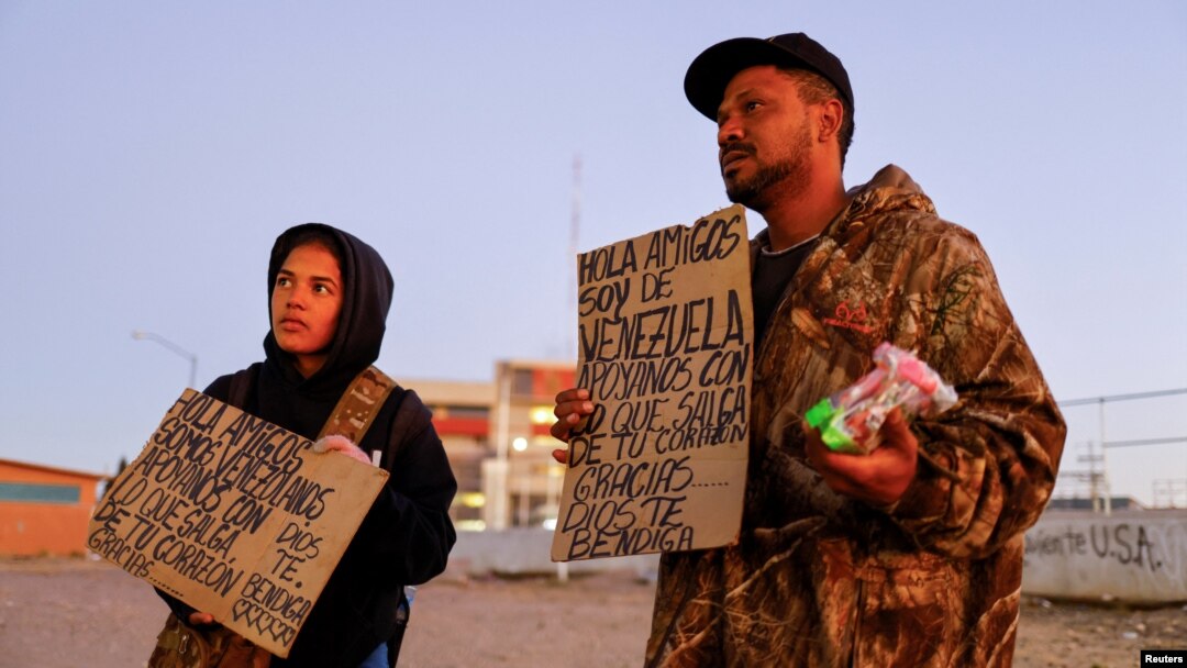 Julio Marquez and Yalimar Chirinos, migrants from Venezuela, display signs near the border between the United States and Mexico, in Ciudad Juarez, Mexico, Jan. 7, 2023. The signs reads "Hello friends, we are from Venezuela, support us with what comes out from your heart."