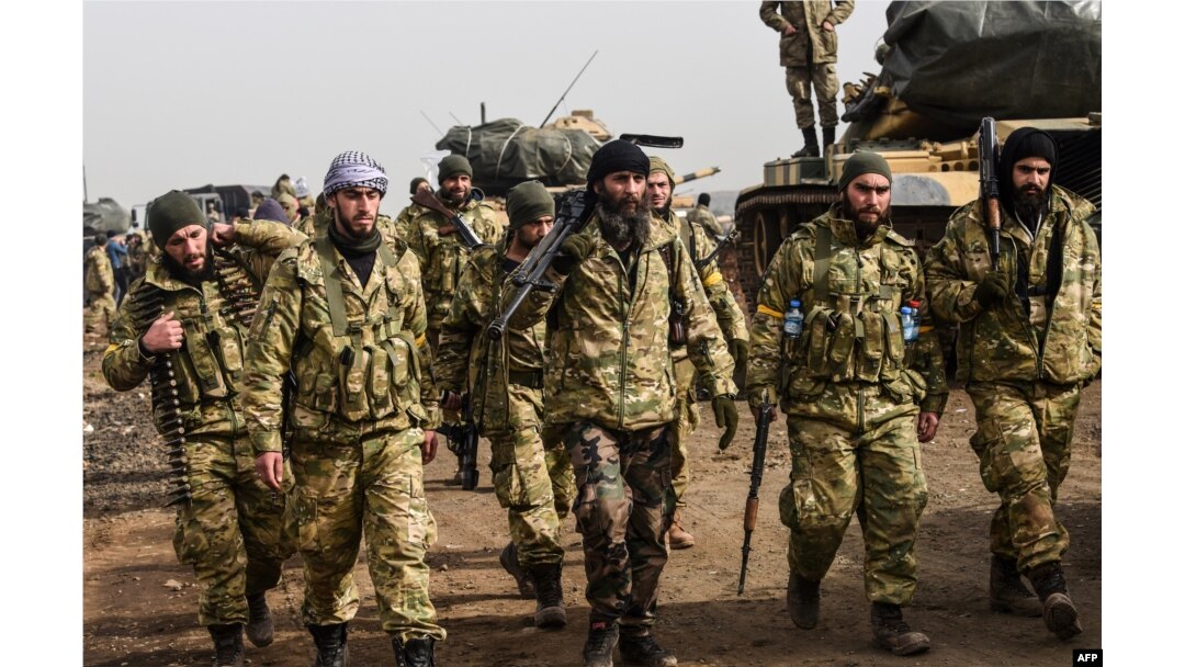 Syrian opposition fighters backed by Turkey walk in front of Turkish troops near the Syria border at Hassa, Hatay province on Jan. 22, 2018.