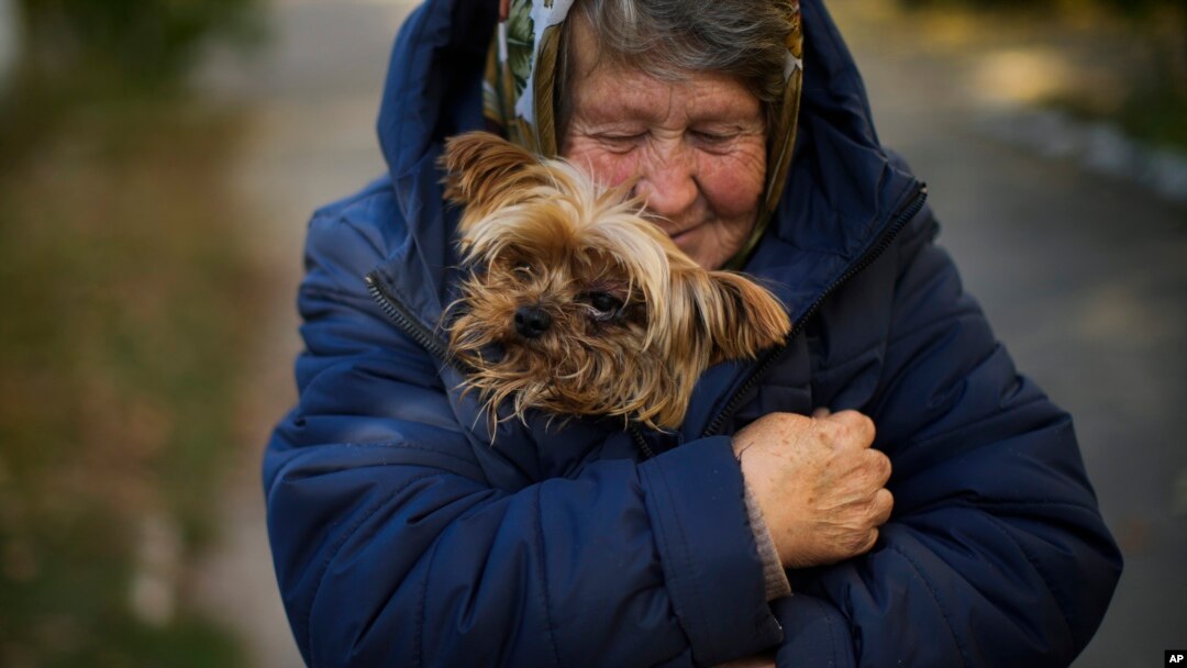A woman warms her dog in Kivsharivka, Ukraine, Oct. 16, 2022. As temperatures drop in Ukraine, those who haven't fled the Russian occupation are on the threshold of winter. The UNHCR has launched a global campaign to help people displaced by war and persecution survive winter.