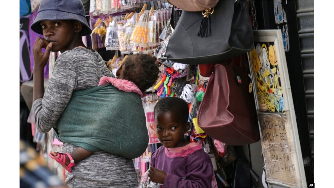 FILE - A woman with two children walks through the busy Bara Taxi Rank in Soweto, South Africa, April 5, 2022.