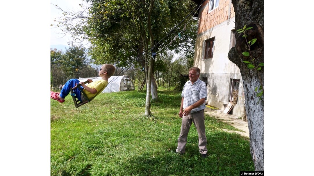 Huso Ahmić, now 72 years old, plays with a grandson in the garden of his family home, which was rebuilt after it was razed in the 1993 attack. His parents died in the blaze.