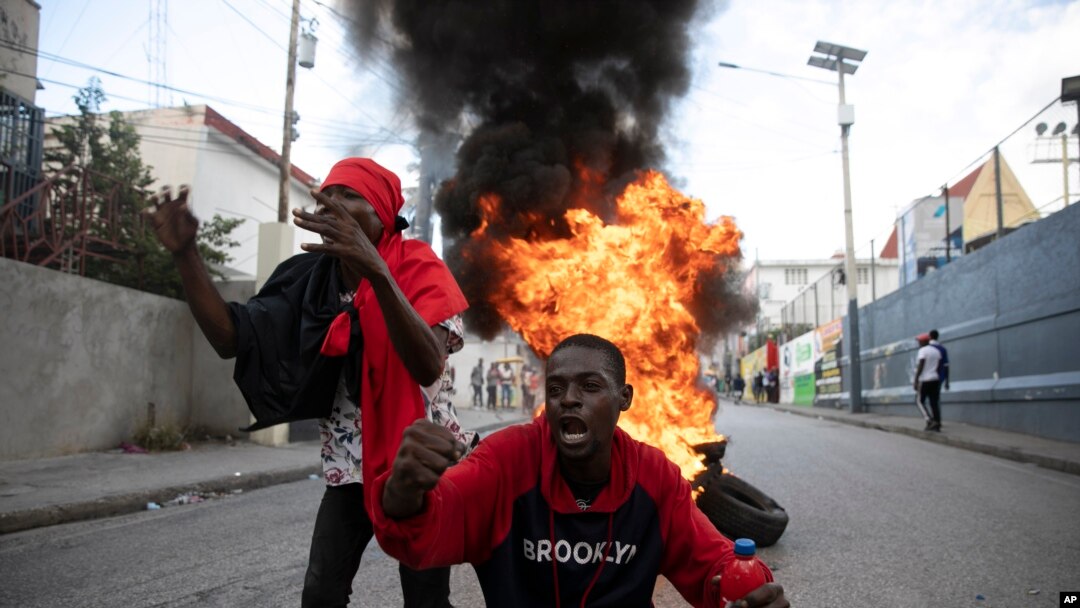 Manifestantes gritan consignas contra el gobierno frente a una barricada de neumáticos en llamas durante una protesta, el viernes 18 de noviembre de 2022, en Puerto Príncipe, Haití. 