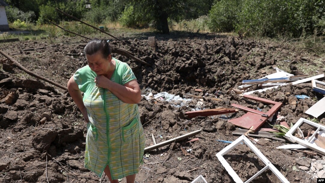 A woman reacts next to a crater caused by Russian bombardments outside her house in the town of Toretske, in Ukraine's Donetsk region, July 17, 2022.