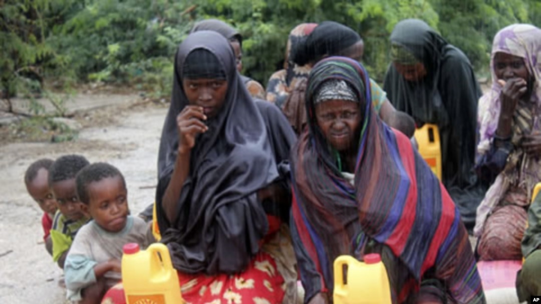 Somali women and children from southern Somalia wait in the rain with some basic rations at a displaced camp in Mogadishu, Somalia, July 15, 2011