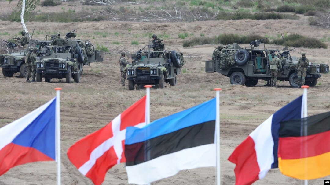 FILE - Flags wave in front of soldiers taking positions with their army vehicles during the NATO Noble Jump exercise on a training range near Swietoszow Zagan, Poland, June 18, 2015.