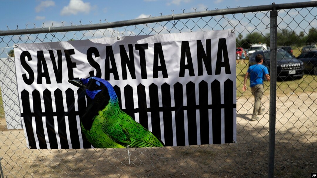 A man walks past a sign in support of Santa Ana National Wildlife Refuge, home to 400-plus species of birds and several endangered wildcats, at a rally in Mission, Texas, Aug. 12, 2017.