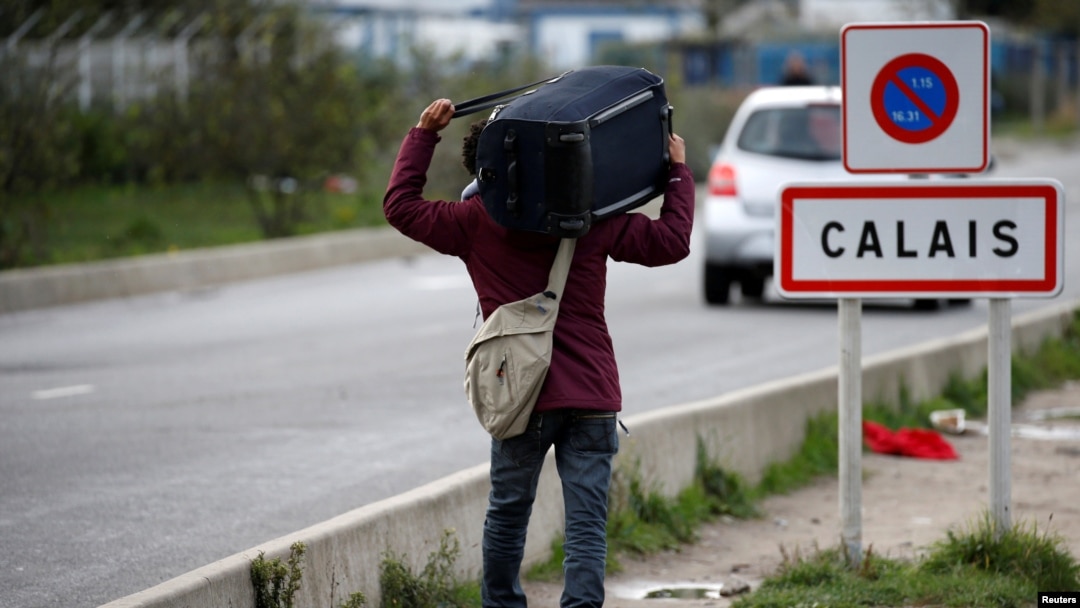 FILE - A migrant carries his belongings as he departs a camp in Calais, France, Oct. 22, 2016.