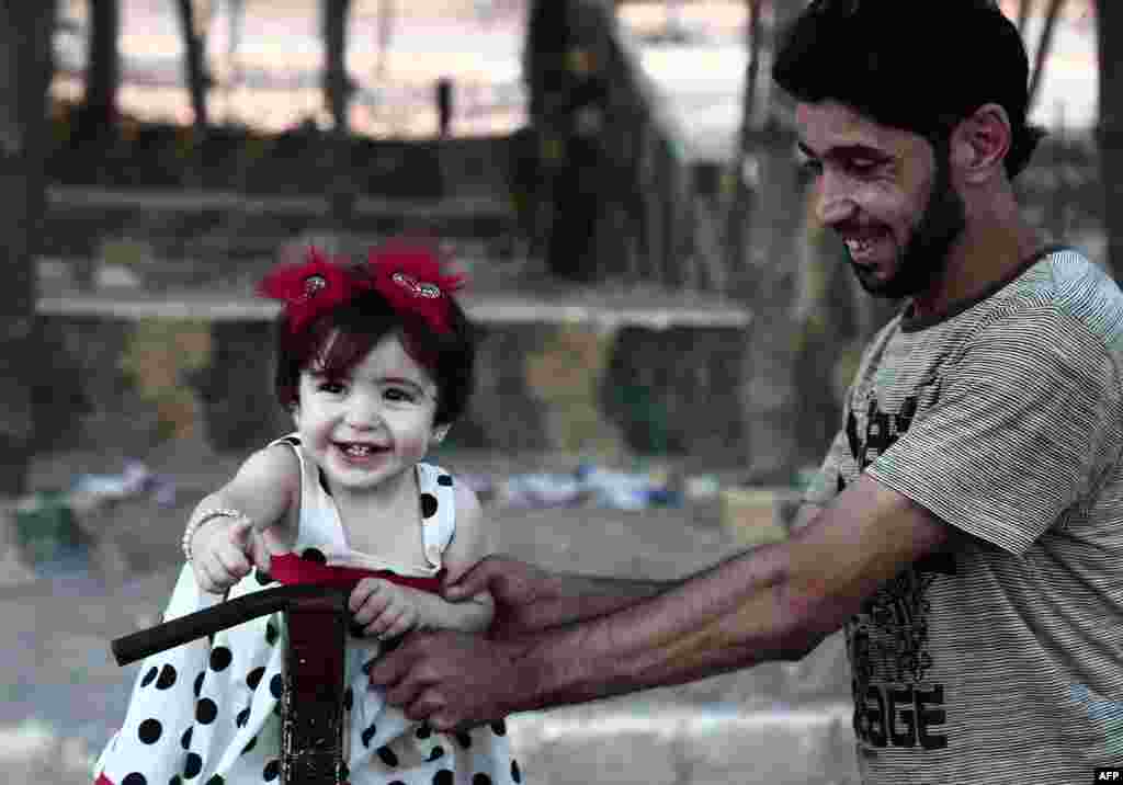 A man plays with a child dressed in her holiday clothes on the second day of Eid el-Adha at a park in the Syrian city of Afrin, Aug. 22, 2018.