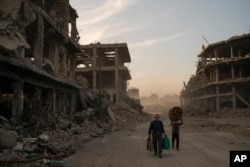 FILE - Residents carry belongings they collected from their damaged house to wash before returning to live in the Old City of Mosul, Iraq, Nov. 15, 2017.