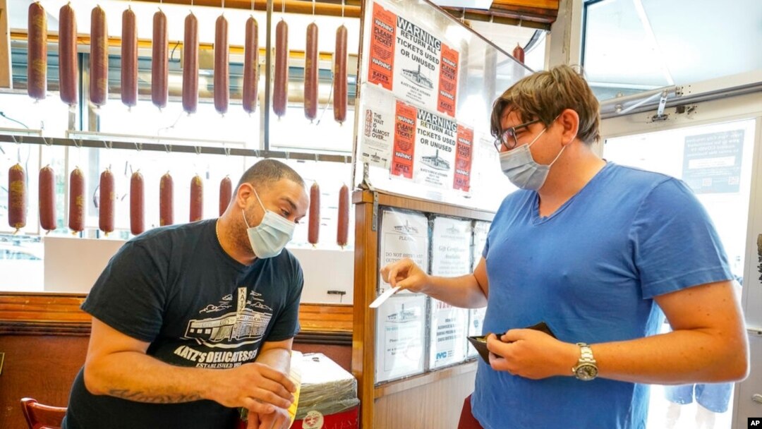 A Katz's Deli employee, left, checks the proof of vaccination from a customer who will be eating inside the restaurant, in New York, Aug. 17, 2021.