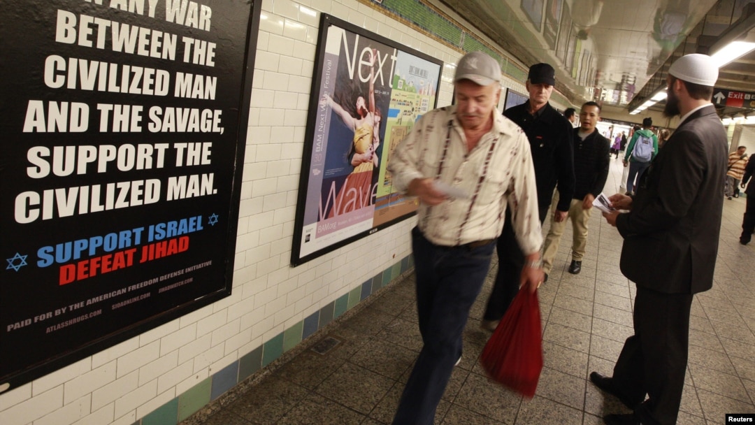 FILE - Cyrus McGoldrick, a member of the Council on American-Islamic Relations, talks to commuters as they walk by an advertisement that reads "Support Israel/Defeat Jihad" in the Times Square subway station in New York, Sept. 24, 2012.
