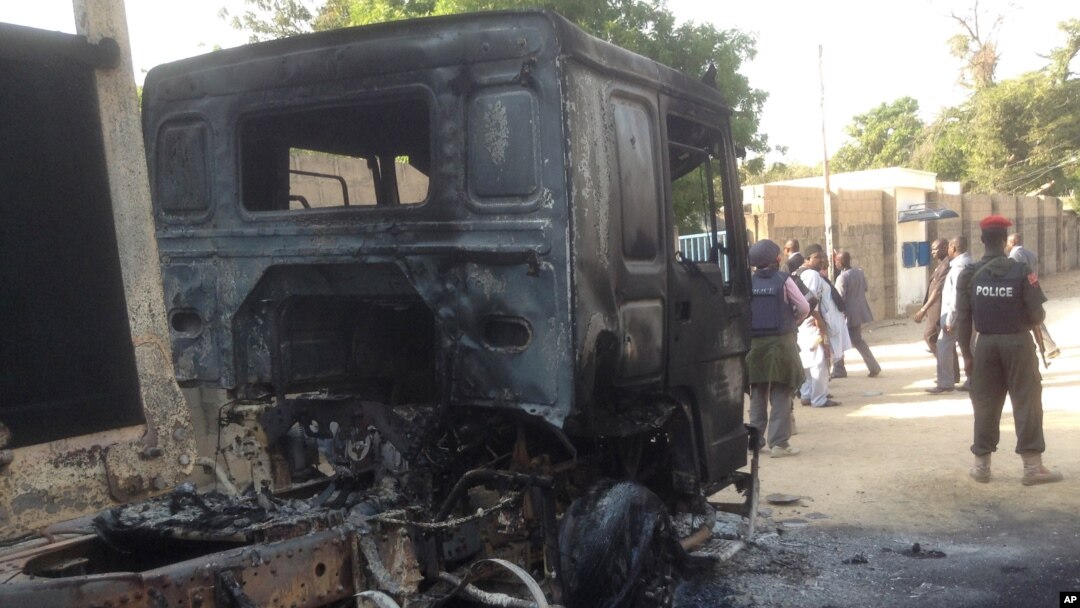 In this photo taken with an iPad policemen stand guard at a burned out truck following an attack by Boko Haram Islamists near an air force base in Maiduguri, Nigeria, Dec, 2. 2013.