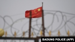 (FILES) This file photo taken on June 4, 2019 shows the Chinese flag behind razor wire at a housing compound in Yangisar, south of Kashgar, in China's western Xinjiang region. 