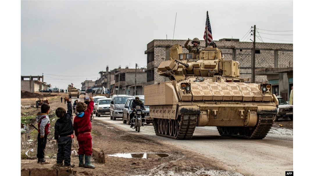 FILE - Children greet a U.S. soldier atop a Bradley Fighting Vehicle as U.S. troops patrol in the Syrian town of al-Jawadiyah in the northeastern Hasakeh province, Dec. 17, 2020.