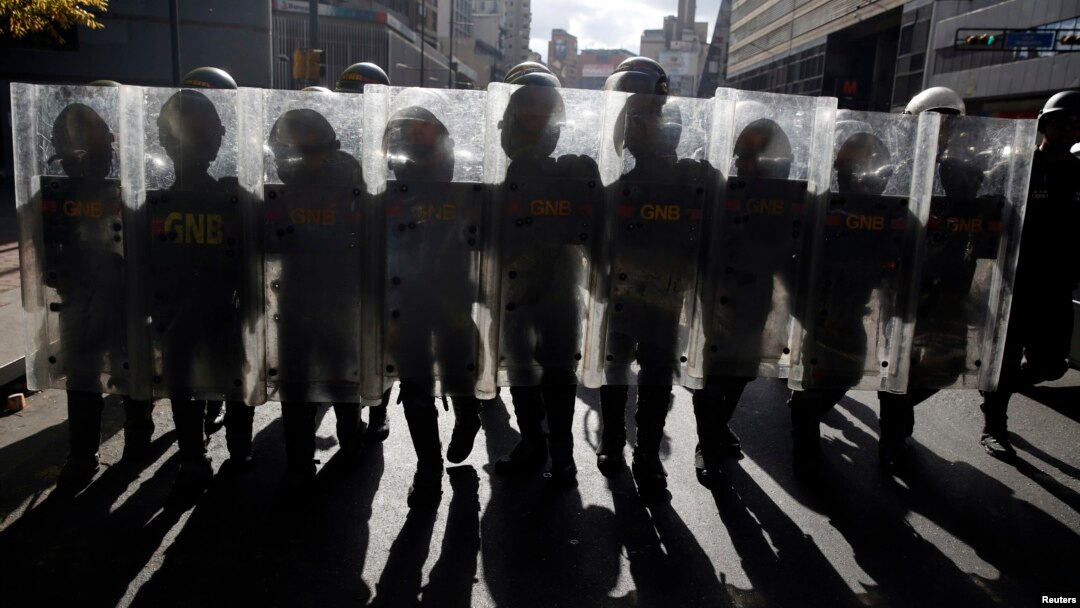 File - National Guards walk with their shields up as they keep guard during a street protest in Caracas, Feb. 18, 2015. 