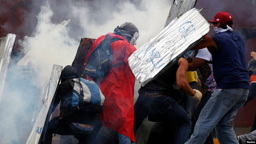 Estudiantes se protegen de los gases lacrimógenos lanzados por la Guardia Nacional al finalizar las protestas del domingo, en Caracas .