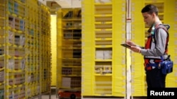 FILE - An employee works next to drive units robots at the Amazon fulfilment center in Bretigny-sur-Orge near Paris, France, October 22, 2019.