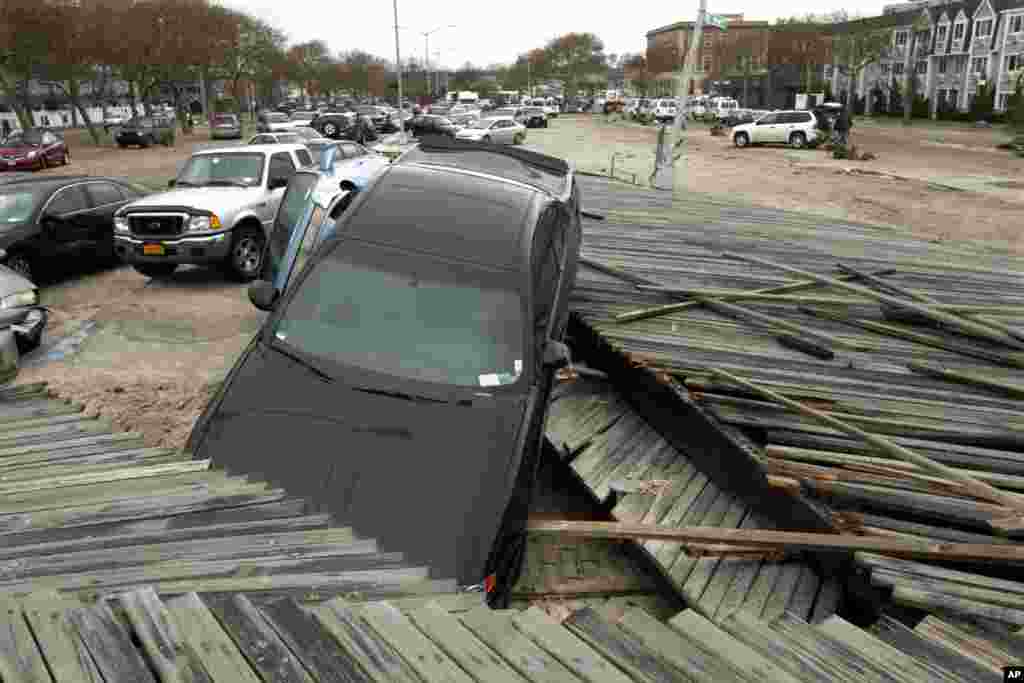 Pedestrians walk past the boardwalk and cars displaced by superstorm Sandy, near Rockaway Beach in the New York City borough of Queens, Oct. 30, 2012, in New York.