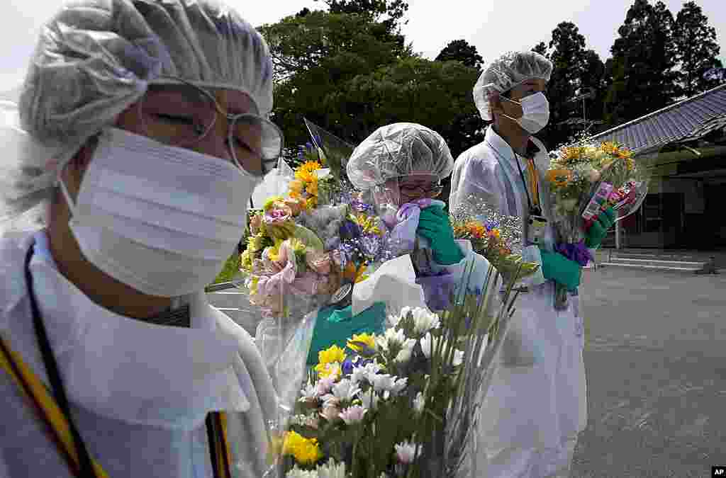 Mourners in protective suits hold flowers at a memorial ceremony for residents from the town of Okuma, inside the contaminated exclusion zone near the crippled Fukushima Daiichi nuclear power plant, July 24, 2011. 