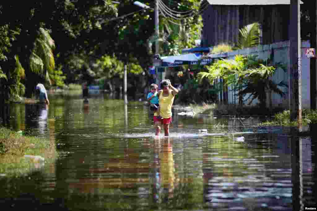 A woman carries a child while walking through a flooded neighborhood in Acapulco, Sept. 18, 2013. 
