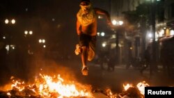 A demonstrator jumps over trash set afire during protests against poor public services, police violence and government corruption, in Sao Paulo, Brazil, June 18, 2013. 