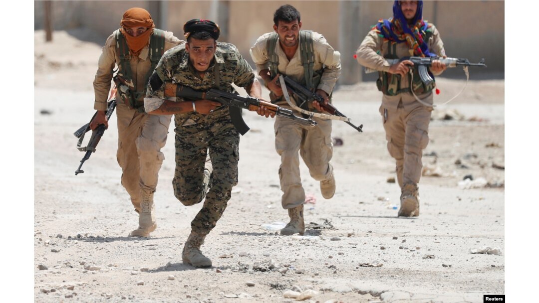 FILE - Kurdish fighters from the People's Protection Units (YPG) run across a street in Raqqa, Syria, July 3, 2017.