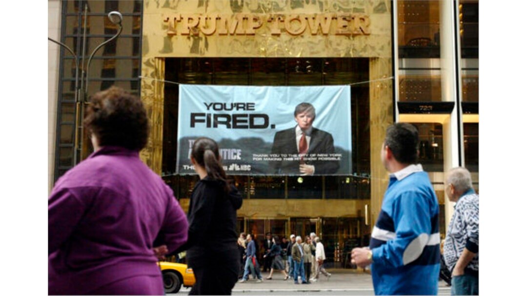 FILE - In this Saturday, March 27, 2004 file photo, passersby look at a sign advertising the reality television show, "The Apprentice," displayed at the entrance to the Trump Tower building in New York.