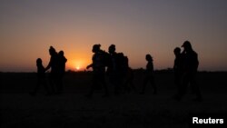 El sol sale mientras familias de migrantes en busca de asilo de Honduras y El Salvador caminan hacia el muro fronterizo, después de cruzar el río Grande hacia Estados Unidos desde México en una balsa, en Peñitas, Texas, Estados Unidos, el 26 de marzo de 2021. 