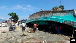 Habitantes observan un barco que fue arrastrado a la costa por el tsunami que asoló el área de Palu, en la provincia de Sulawesi Central en Indonesia, el domingo 30 de septiembre de 2018.