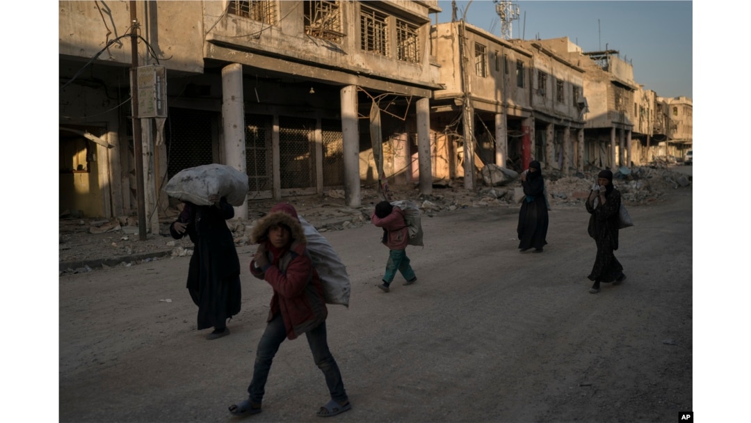 FILE - Children and women carry metal scraps they collected from the rubble in the Old City of Mosul, Iraq, Nov. 16, 2017.