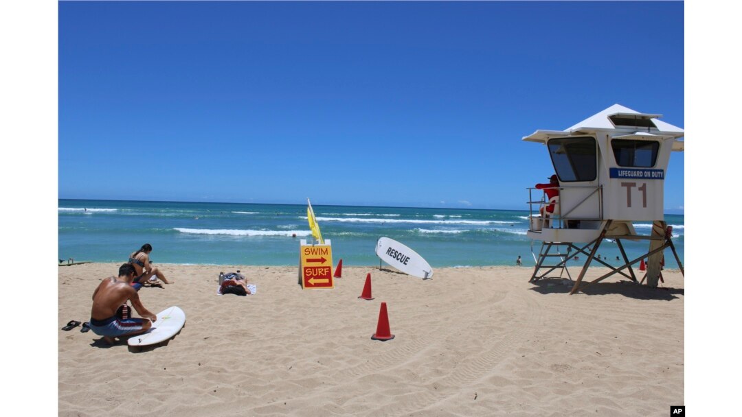A surfer waxes his board on the sand at a beach known as White Plains in Ewa Beach, Hawaii, on May 12, 2023. (AP Photo/Jennifer Sinco Kelleher)