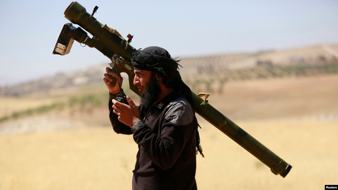 FILE - An Islamist Syrian rebel group Jabhat al-Nusra fighter talks on a walkie-talkie while carrying his weapon on Al-Khazan frontline of Khan Sheikhoun, northern Idlib province, Syria, May 17, 2014. 