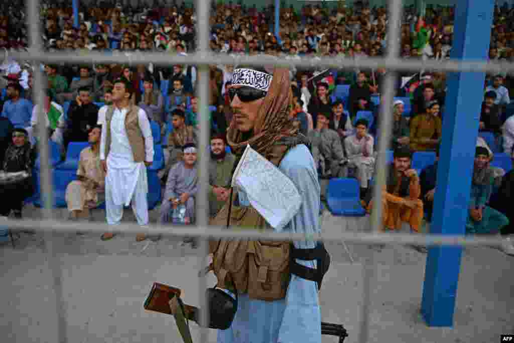 A Taliban fighter, center, keeps vigil as spectators watch the Twenty20 cricket trial match being played between two Afghan teams at the Kabul International Cricket Stadium in Kabul.