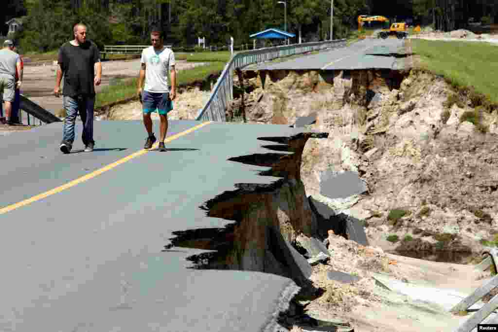 Local residents walk along the edge of a collapsed road that ran atop Patricia Lake's dam in the aftermath of Hurricane Florence, in Boiling Spring Lakes, North Carolina, Sept. 19, 2018.