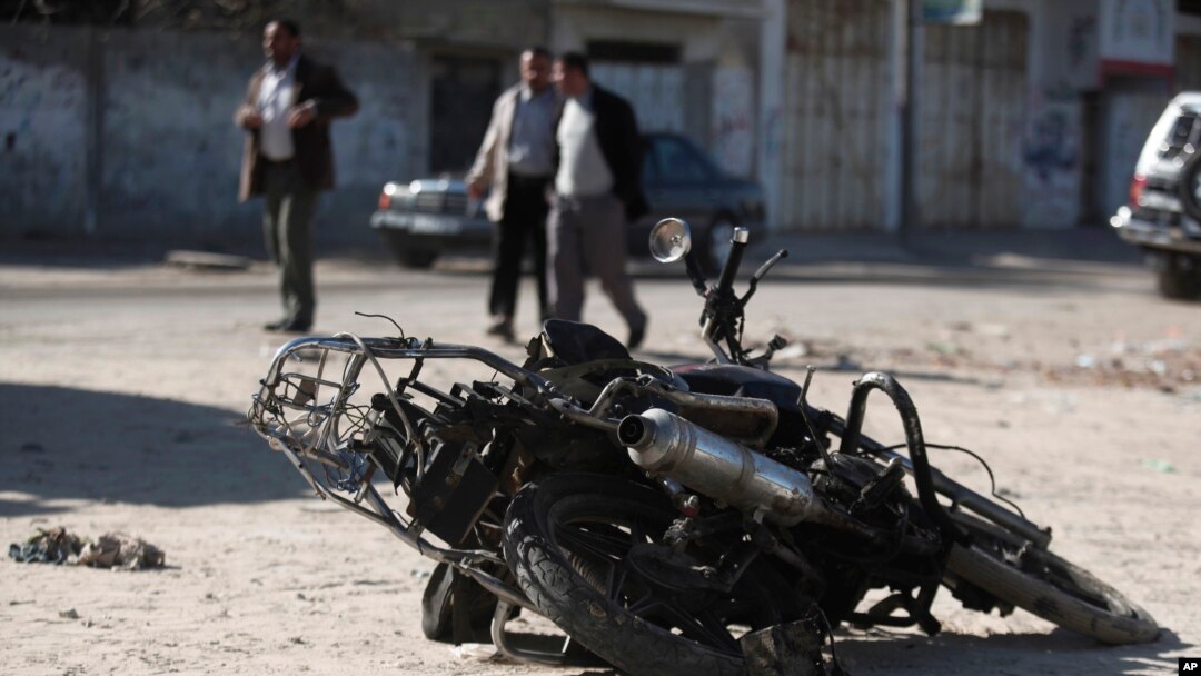 Palestinians walk near the debris of a damaged motorcycle after an Israeli airstrike in Deir al-Balah, central Gaza Strip, Sunday, Feb. 9, 2014. 
