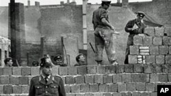 圖為1961年10月7日一名西柏林士兵站立在分割東、西柏林的混凝土牆邊。他身后為東柏林工人正在加高圍牆