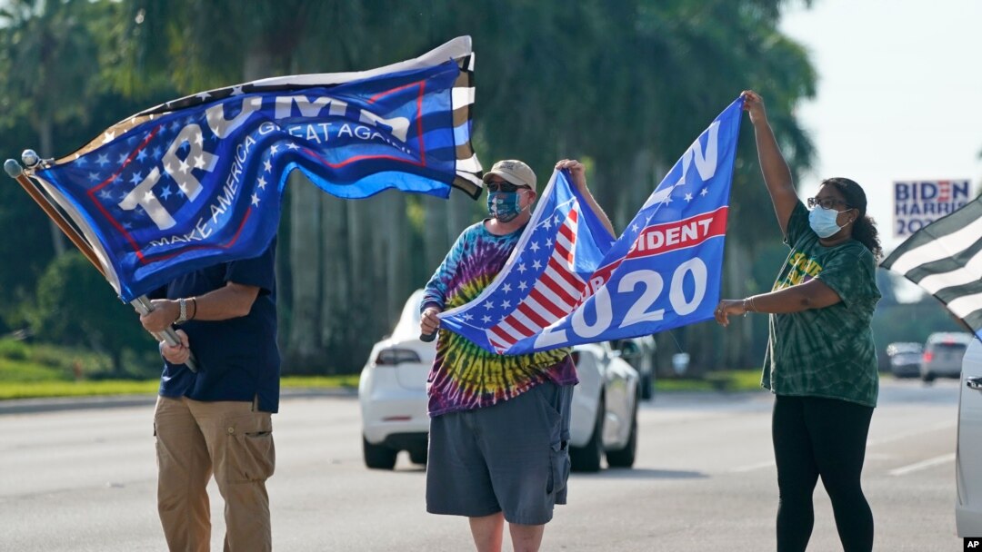 Archivo - Partidarios del presidente Donald Trump y el exvicepresidente demócrata Joe Biden ondean banderas mientras esperan que llegue la caravana de Biden, el 13 de octubre de 2020, en el Parque Regional Miramar en Miramar, Florida.