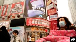 Residents wearing masks past by a screen showing a trailer for the film "Days and Nights in Wuhan" outside a mall in Wuhan in central China's Hubei province on Jan. 22, 2021.