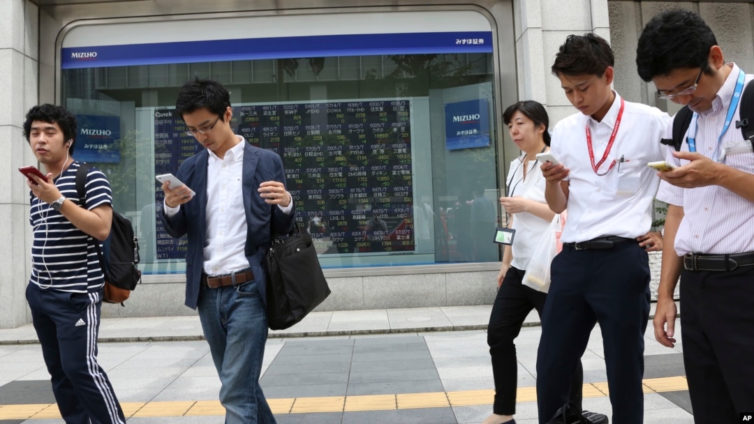 People look at their smartphones in front of an electronic stock board of a securities firm in Tokyo, Monday, Aug. 28, 2017. (AP Photo/Koji Sasahara)