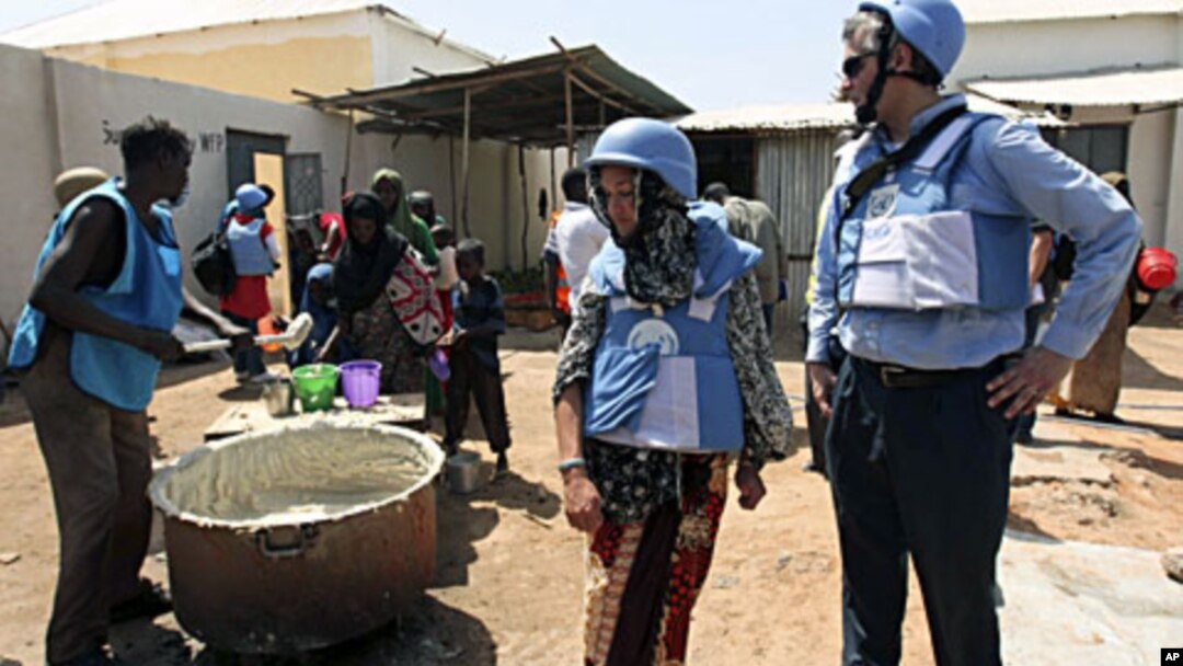 United Nations personnel look on as a worker serves food at a camp in Hodan district in Mogadishu, January 19, 2012