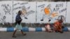 FILE - A man walks past a woman who sits by a wall with graffiti that mocks Indian politicians ahead of the general election in Kolkata, India, Apr. 1, 2019.
