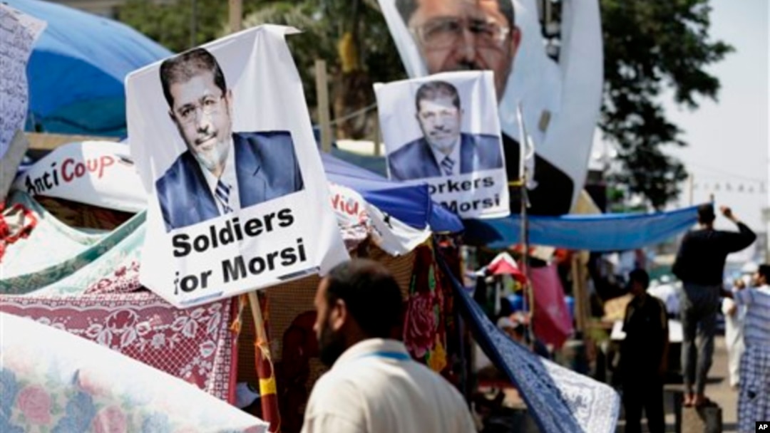 A supporter of Egypt's Islamist President Mohamed Morsi in front pictures of Morsi at Nasr City, where protesters have installed their camp and hold their daily rally, in Cairo, Egypt, July 25, 2013.