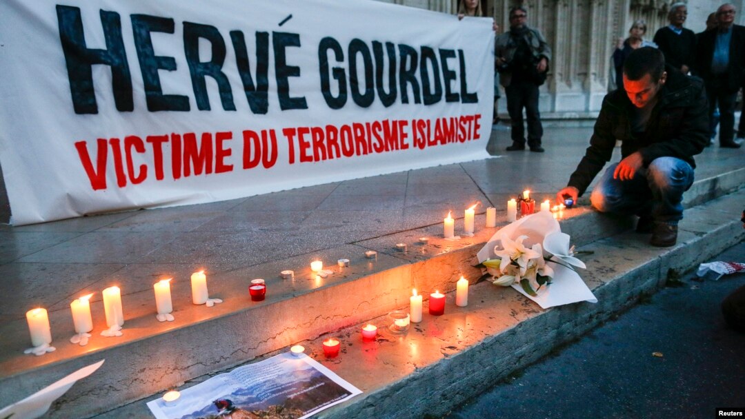 FILE - A man places a candle near a banner as people pay tribute to Herve Gourdel, a French mountain guide who was beheaded by an Algerian Islamist group, in Lyon, France, Sept. 26, 2014.