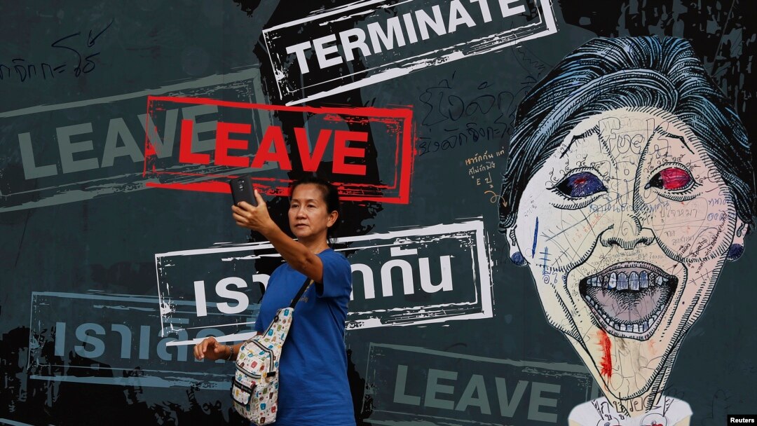 A woman takes a "selfie" in front of a banner with a caricature of the caretaker Prime Minister Yingluck Shinawatra displayed inside an anti-government protest encampment in central Bangkok, Feb. 25, 2014.