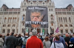 FILE: A man holds a poster of Hungarian Premier Viktor Orban that reads "What have I done again" during a protest by opposition parties against Orban's policies on migrants in Budapest, Hungary, Oct. 2, 2016.